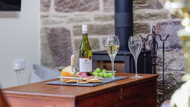 A wooden table with a bottle of wine, two glasses, cheese, and grapes.