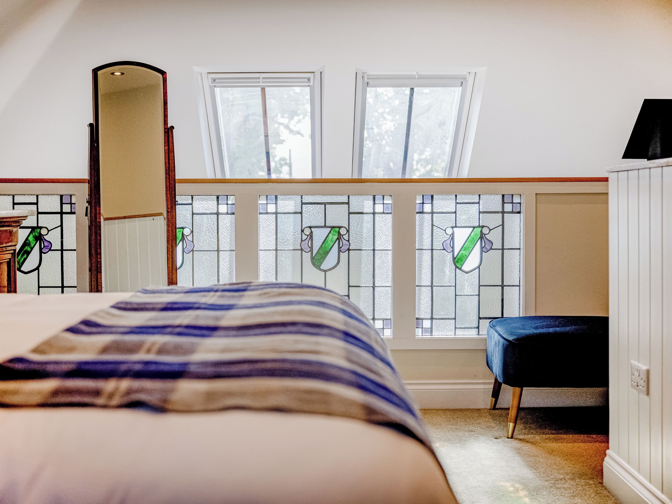 Een slaapkamer met een bed, een stoel, een spiegel en een raam met glas-in-lood.
