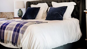 A neatly made bed with a white and blue plaid blanket, a dark headboard, and two dark pillows.