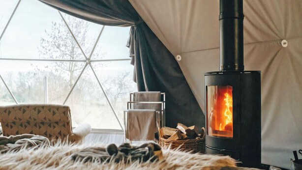 A cozy tent with a wood-burning stove, a cushioned chair, and a furry rug. - The Star Dome - UKC6978 (Ludlow)