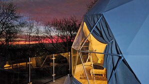 A dome-shaped tent with a clear interior, a bed, and a view of the landscape. - The Star Dome - UKC6978 (Ludlow)