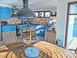 A modern kitchen with blue cabinets, a wooden table, and a view of the outside. - Flag House - UKC7074 (Brundall)