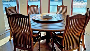 A dining area with a round table and six wooden chairs, large windows with a view of a body of water and buildings, and a black pendant light above the table. - Flag House - UKC7074 (Brundall)