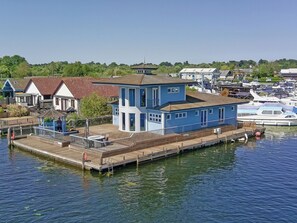 A waterfront property with a dock, a small building with a balcony, and boats in the background. - Flag House - UKC7074 (Brundall)