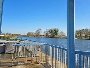 A wooden dock with metal railings, a lifebuoy, and wicker furniture. - Flag House - UKC7074 (Brundall)