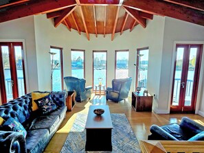 A spacious living room with a high ceiling, large windows, and a view of a body of water. - Flag House - UKC7074 (Brundall)