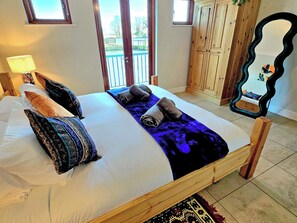 A bedroom with a bed, pillows, a nightstand, a mirror, and a view of the outdoors. - Flag House - UKC7074 (Brundall)