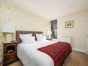 A bedroom with a large bed, two bedside tables, a radiator, and a window with a view.