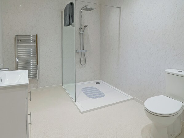 Ein modernes Badezimmer mit einer Duschkabine, einer weißen Toilette und einem Waschbecken mit Handtuchhalter.