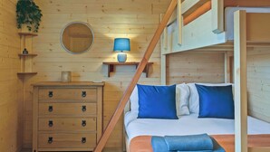 A wooden cabin interior with a bunk bed, a dresser with bear-shaped handles, a mirror, and a lamp. - Ferry Lodge - UKC7073 (Brundall)