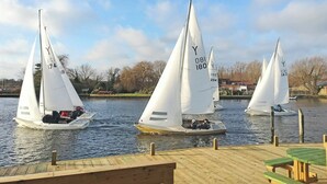 Three sailboats on a calm body of water, docked at a wooden pier with picnic tables. - Ferry Lodge - UKC7073 (Brundall)