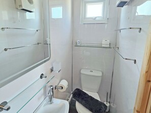 A compact bathroom with a toilet, a sink, a mirror, and a small window. - Dinky Daze - UKC7071 (Brundall)