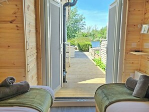 A wooden cabin with two beds, a wooden deck, and a view of a lake. - Dinky Daze - UKC7071 (Brundall)