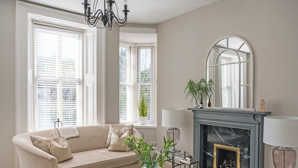 A living room with a beige sofa, a glass coffee table, a fireplace, and large windows with blinds. - 2 bedroom accommodation in Birnam (Birnam)