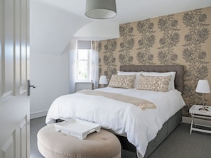 Une chambre à coucher avec un grand lit, une table de chevet avec une lampe, une fenêtre avec des rideaux et un papier peint à motifs.