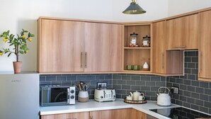 A modern kitchen with wooden cabinets, a built-in oven, a toaster, and a kettle on the countertop. - 2 bedroom accommodation in Birnam (Birnam)