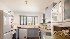 Eine kleine Küche mit Waschmaschine, Geschirrspüler und einem Fenster mit Jalousien.