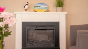 A modern living room with a fireplace, a decorative shelf with a pufferfish figurine, a painting of a beach, and a small plant. - 18 Ocean Terrace - UKC7117 (Ilfracombe)