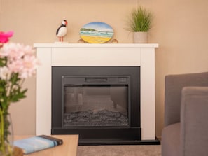 Ein modernes Wohnzimmer mit Kamin, einem dekorativen Regal mit einer Kugelfisch-Figur, einem Strandbild und einer kleinen Pflanze.