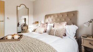 A neatly arranged bedroom with a large bed, a bedside table, a lamp, and a mirror.