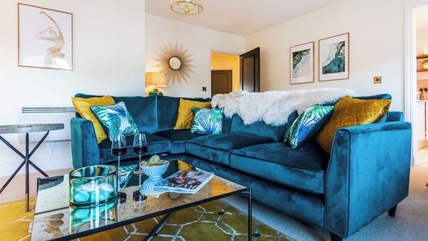 A modern living room with a blue sectional sofa, a glass coffee table, and a sunburst mirror on the wall. - 2 bedroom accommodation in Warwick (Warwick)