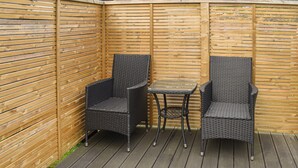 En hyggelig hjørne terrasse med to fletstole og et lille bord.