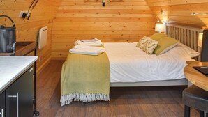 Et hyggeligt rum med træpaneler, seng, lille bord og hængende lampe.