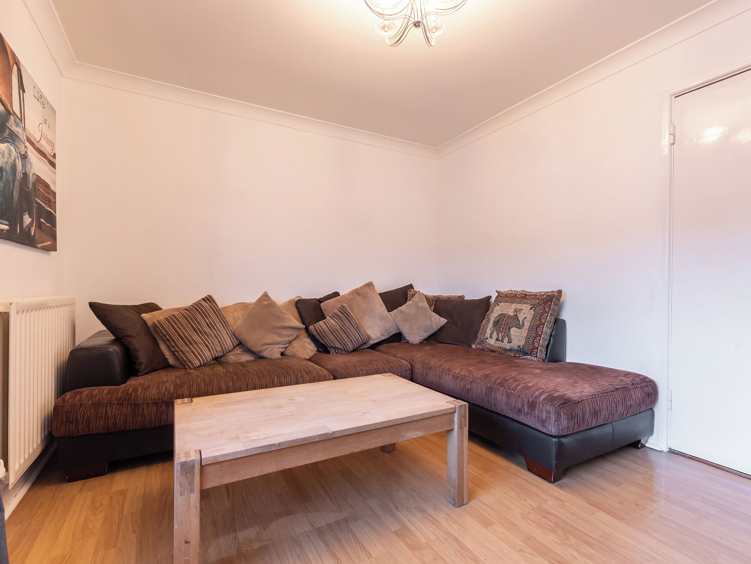 Ein modernes Wohnzimmer mit einem braunen Ecksofa, einem Holztisch und einem weißen Heizkörper.