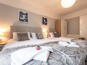 Habitación de hotel con dos camas, cada una con cabecero y un edredón grande. Dos lámparas de pared a cada lado de las camas, y un armario de madera en la esquina.