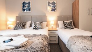 Ein Hotelzimmer mit zwei Betten, jedes mit gemusterten Kissen, Nachttischen inklusive Lampen und Bildern an den Wänden.