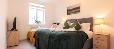 A bedroom with a bed, bedside tables, a TV, a window, and a painting on the wall.