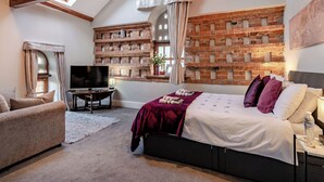 Een slaapkamer met een bakstenen muur, een bed met kussens, een televisie en een raam met gordijnen.
