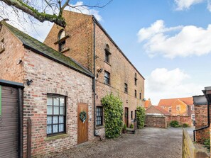 A traditional brick building with a gravel courtyard, wooden doors, and a brick chimney. - 1 bedroom accommodation in Bilbrough, near York (Bilbrough, near York)