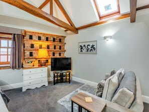 A cozy living room with a brick wall, a flat-screen TV, a wooden coffee table, and a sofa with cushions. - This peaceful position is surrounded by beautiful countryside and walks. (Bilbrough, near York)