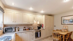 Una cocina con armarios blancos, un microondas, un tostador y una mesa de comedor de madera con sillas.