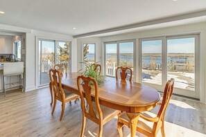 Ein Essbereich mit Holztisch und Stühlen, große Fenster mit Blick auf Wasser und Bäume, sowie eine Küchenzeile mit Spüle und Arbeitsfläche.