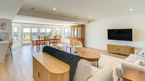 Amplia sala de estar con un gran ventanal con vista al mar, un mueble de madera, un televisor de pantalla plana y una zona de estar acogedora.