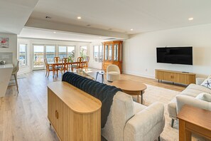 Een ruime woonkamer met een groot raam met uitzicht op zee, een houten kast, een flatscreen televisie en een gezellige zithoek.