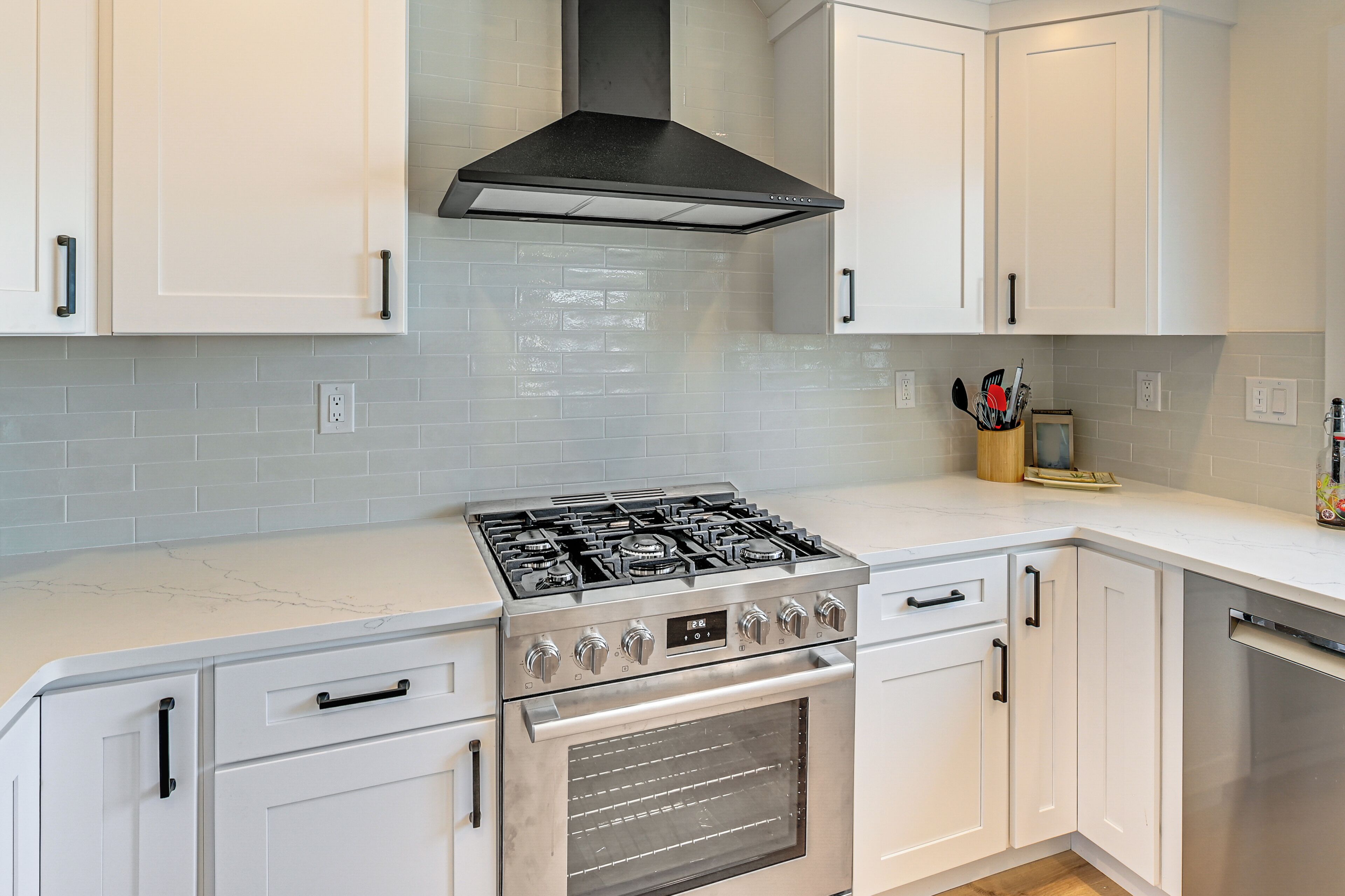 Una cocina con gabinetes blancos, estufa de acero inoxidable y campana extractora negra.
