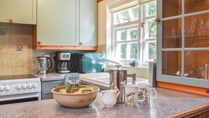 A kitchen with a stove, coffee maker, toaster, and a window with a view of greenery. - 2 bedroom accommodation in Winfrith Newburgh (Winfrith Newburgh)