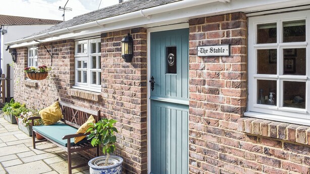 A brick building with a blue door, a bench, and hanging flower baskets. - 2 bedroom accommodation in Winfrith Newburgh (Winfrith Newburgh)