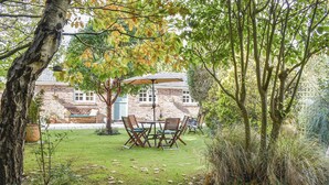 A patio with a table and chairs, surrounded by trees and a brick building in the background. - 2 bedroom accommodation in Winfrith Newburgh (Winfrith Newburgh)