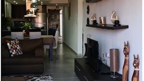 Una sala de estar moderna con un sofá, una mesa de centro y elementos decorativos. Se ve una cocina al fondo con un comedor.