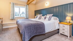 A bedroom with a bed, a nightstand, a lamp, a window with curtains, and a wooden ceiling beam.