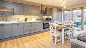 A modern kitchen with grey cabinets, a herringbone backsplash, and a dining area with white chairs and a wooden table.