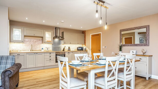 Een moderne keuken met witte kasten, een eettafel met witte stoelen en een houten vloer.