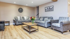 Een woonkamer met twee grijze banken, een houten salontafel en een klok aan de muur.