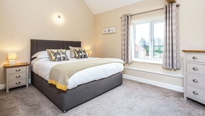 Een slaapkamer met een bed, nachtkastjes, een dressoir, een raam met gordijnen, en een foto aan de muur.