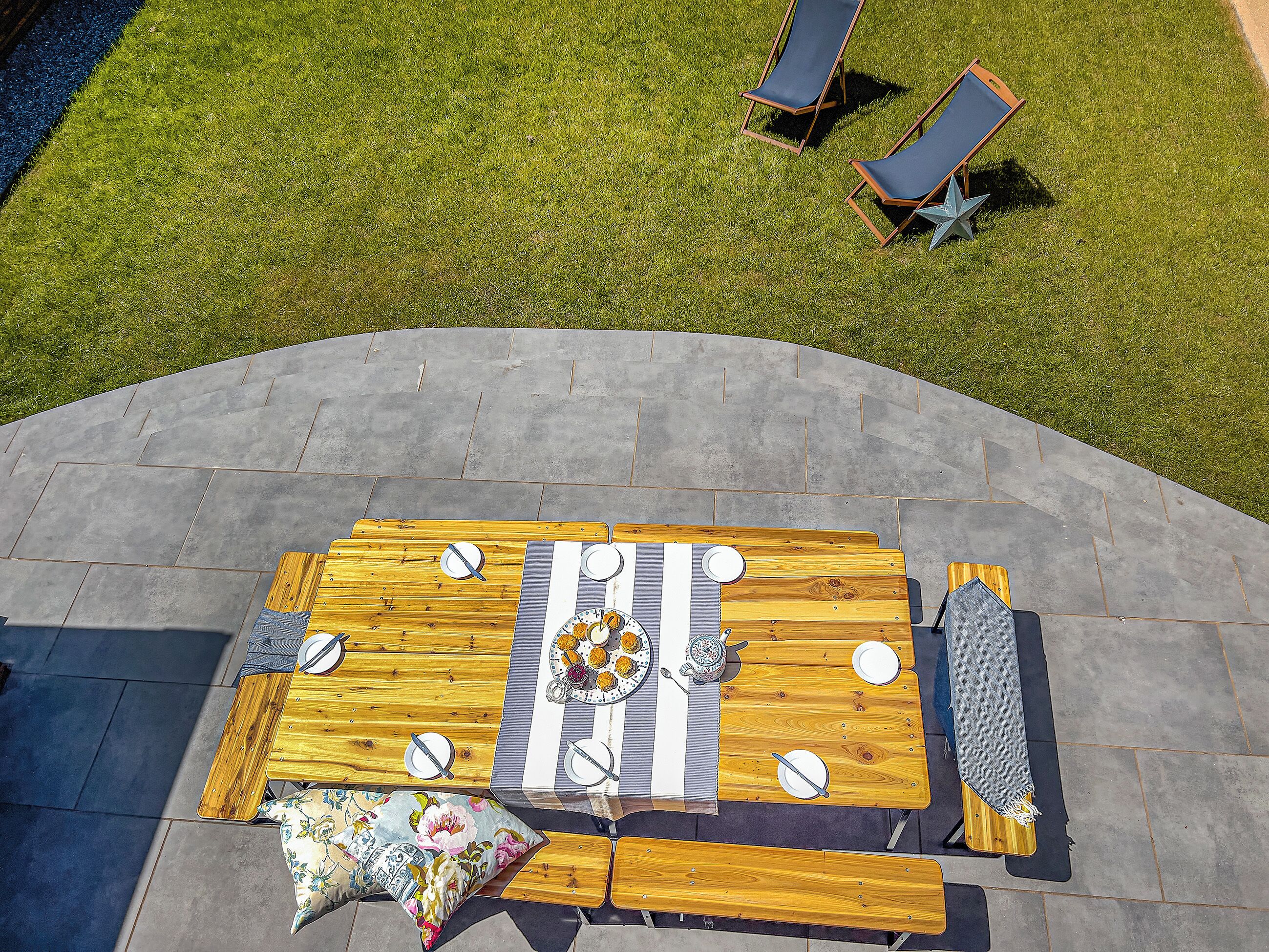 Un espace de restauration en plein air avec une table en bois dressée pour quatre personnes, entourée de chaises et d’un banc.