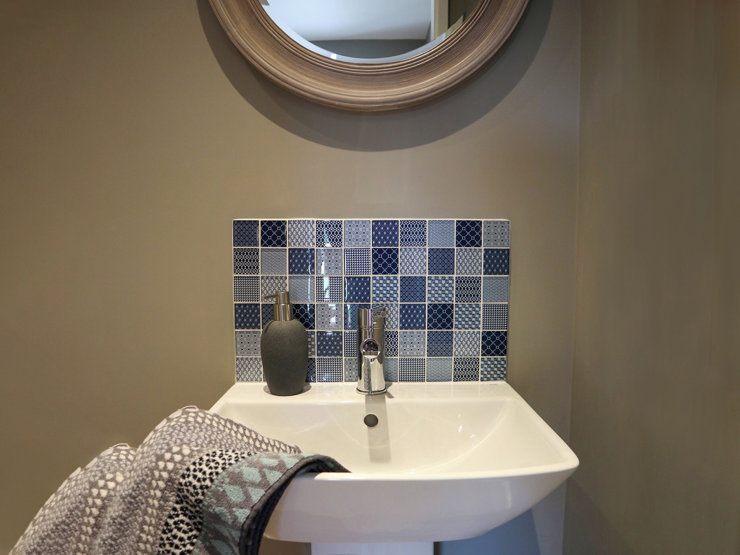 Un baño con un lavamanos blanco, un espejo encima y una salpicadera de azulejos.